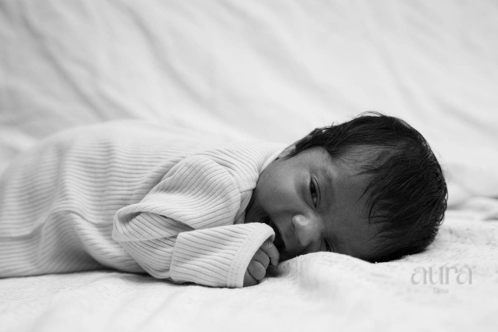A newborn asleep on white bedding, in black and white