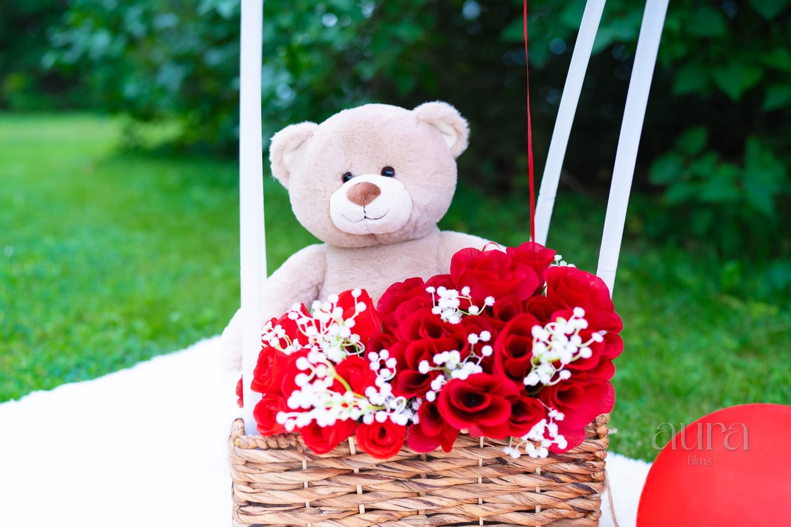 A teddy bear and a basket of red roses decorate an outdoor celebration