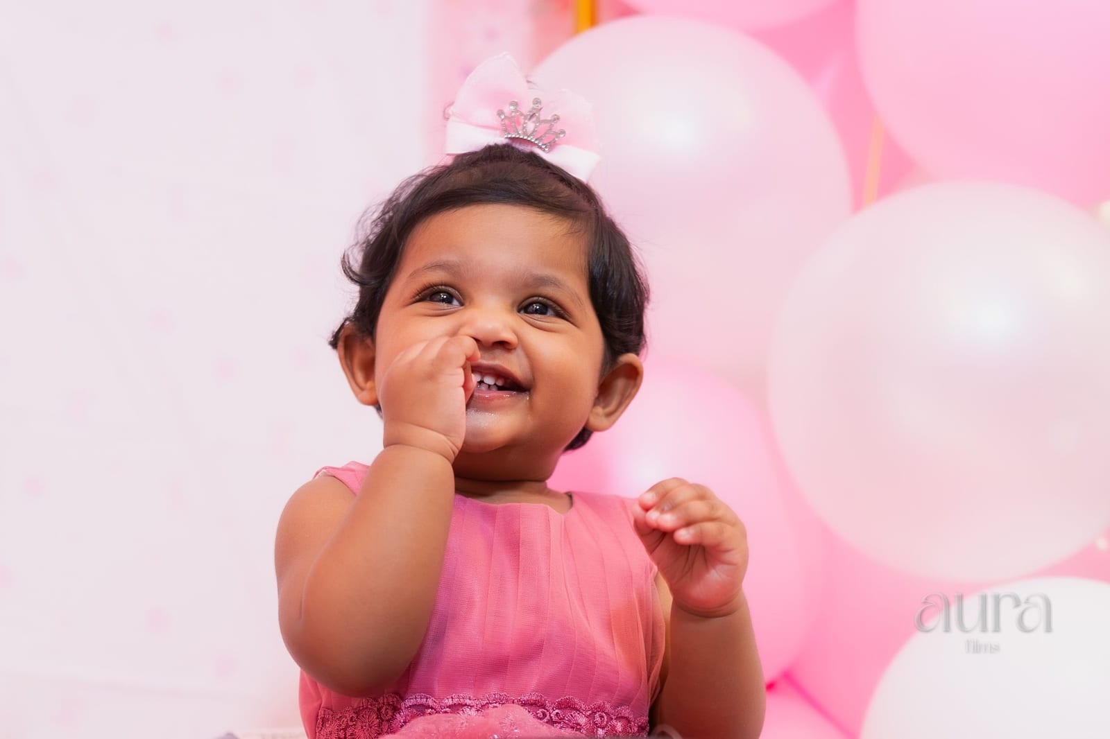 A baby girl in pink laughs among pink balloons at her birthday